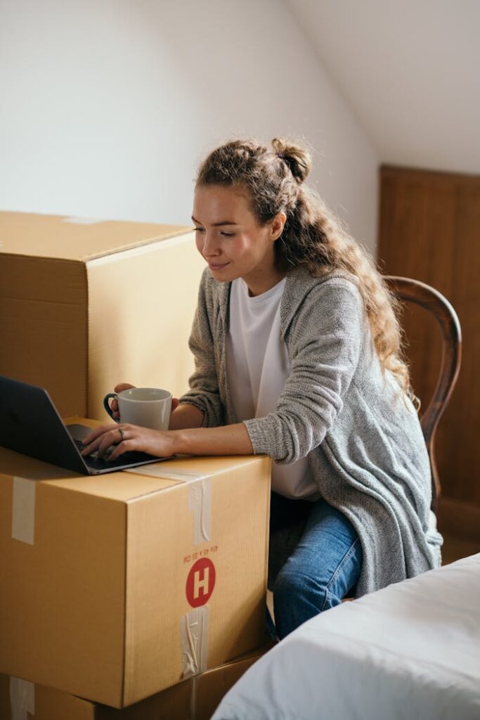 Young woman using laptop while packing boxes in her new home.