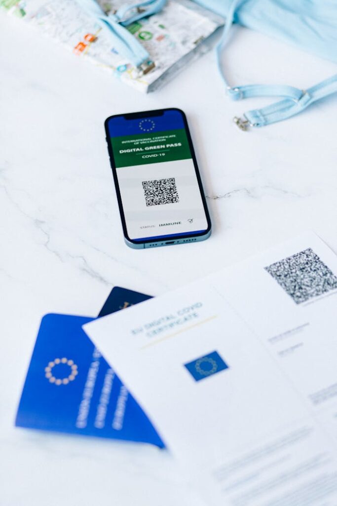 A smartphone displaying a digital vaccine passport alongside Covid-19 documents on a table.